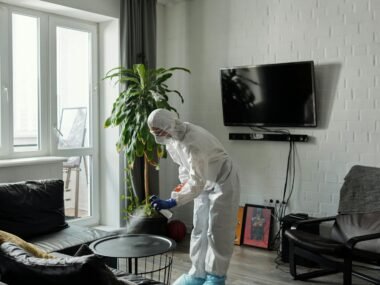 Worker in PPE disinfecting a living room, ensuring safety from viruses.