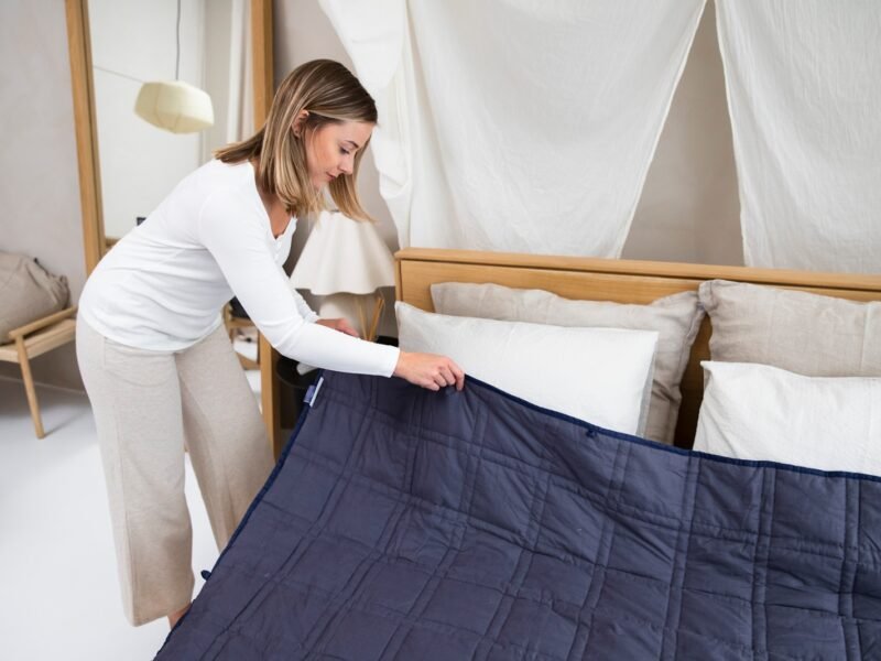 a woman putting a blue blanket on top of a bed